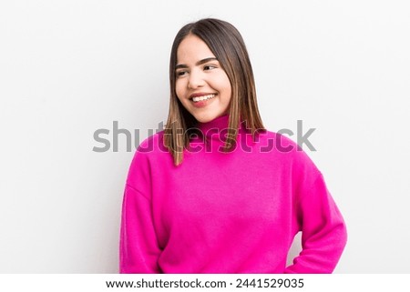 pretty hispanic woman looking happy, cheerful and confident, smiling proudly and looking to side with both hands on hips