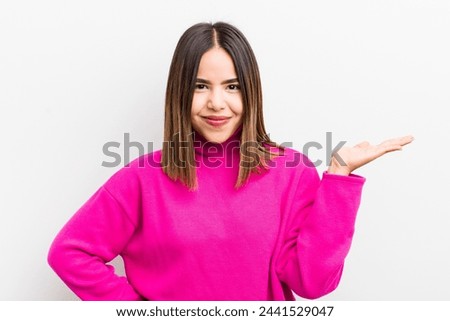 pretty hispanic woman smiling, feeling confident, successful and happy, showing concept or idea on copy space on the side