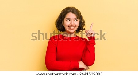 pretty hispanic woman smiling happily and looking sideways, wondering, thinking or having an idea