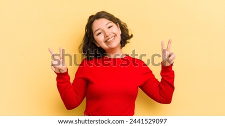 pretty hispanic woman smiling and looking happy, friendly and satisfied, gesturing victory or peace with both hands