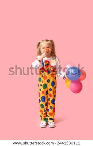 Cute little girl in clown costume with balloons on pink background