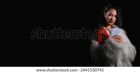 Rich young woman with poker playing cards on black background with space for text