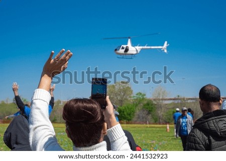 Diverse people hands waving, taking photo hovering helicopter drops colorful eggs, goodies at Easter event, Richardson, Texas, rear view crowd group with mobile phone, holiday Chistian tradition. USA