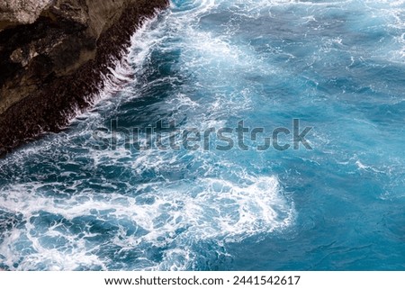 Vibrant blue ocean waters swirl around a rocky coastline, creating white frothy waves