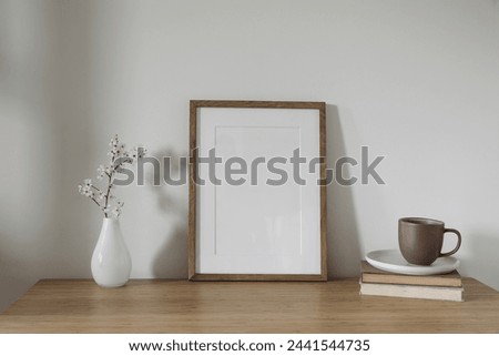 Vertical wooden picture frame, poster mockup. Spring, easter composition. Asian interior, home office still life. Artistic display. Blooming cherry plum tree branches in glass vase. Wooden table.
