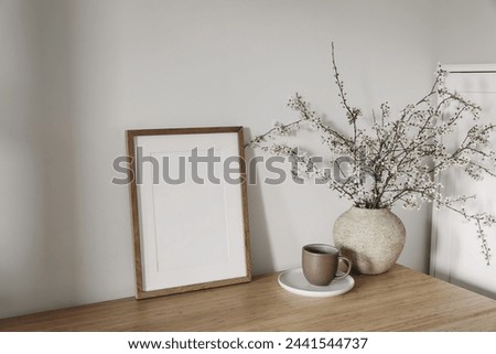 Vertical wooden picture frame, poster mockup in sunlight. Spring, easter composition. Eleganrnterior, home office still life. Blooming cherry plum tree branches in vase. Wooden table, lateral view.