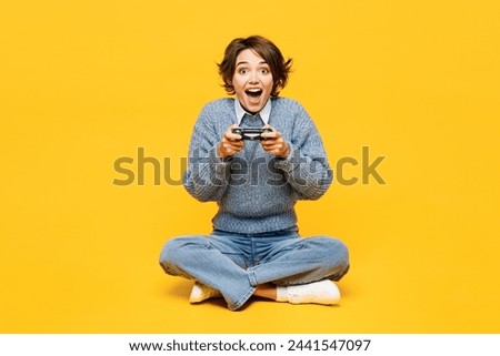 Full body surprised young woman she wears grey knitted sweater shirt casual clothes sits hold in hand play pc game with joystick console isolated on plain yellow background studio. Lifestyle concept