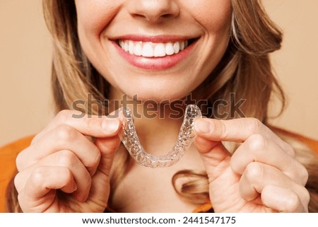 Close up cropped young woman wear orange shirt casual clothes hold in hand invisible transparent aligners, invisalign bracer smile isolated on plain pastel light beige background. Lifestyle concept Royalty-Free Stock Photo #2441547175