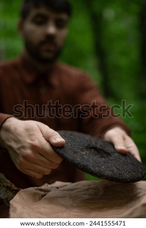 Man holding pressed shu puer tea near craft paper in forest