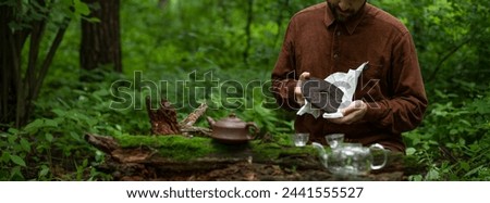 Panoramic shot of man holding round flat disk of shu pu-erh near clay teapot on wooden log with moss