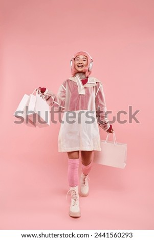 happy asian girl with pink hair and shopping bags in headphones walking on vibrant background