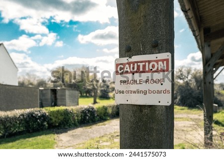 Shallow focus of a Caution sign attached to a wooden barn post. The roof is made of asbestos and is fragile causing injury.