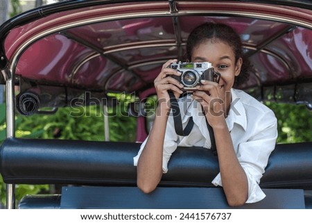 Black traveler woman taking camera and sitting on back seat tuktuk exploring Thailand during summer vacation