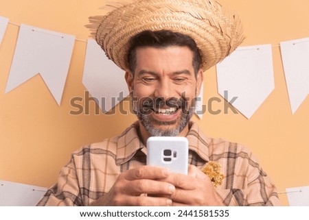 happy mature man to Brazilian Festa Junina in beige studio background. watching video and photos on mobile smartphone