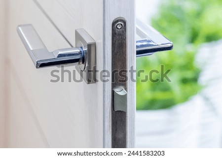 Chrome handle and lock on an open interior door, close-up. Modern door fittings. Minimalism in design. Modern design. Interior accessories for apartments or offices Royalty-Free Stock Photo #2441583203
