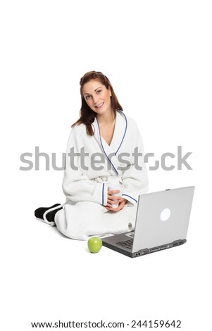 A cute woman in her 20s sitting down on the floor wearing a bathrobe, watching a computer monitor. White background.