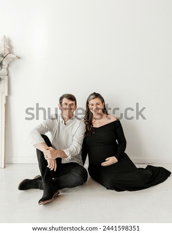 Smiling couple in chic attire during maternity shoot.