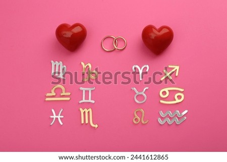 Zodiac compatibility. Signs, wedding rings and red hearts on pink background, flat lay Royalty-Free Stock Photo #2441612865