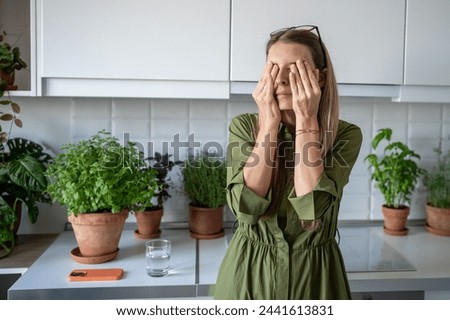 Sleepy woman suffering from insomnia rubbing eyes on kitchen at home early morning. Blonde tired female feeling bad from lack of sleep, headache, migraine, cephalalgia, premenstrual syndrome concept.  Royalty-Free Stock Photo #2441613831