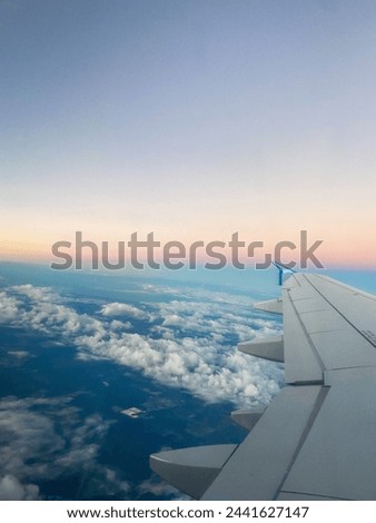 Aircraft wing over cloud-covered landscape at dusk. Aerial travel photography with pastel sky. Journey and adventure concept.