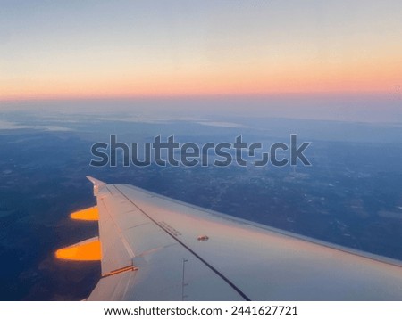 Airplane wing illuminated by sunset light with view over the landscape. Aerial travel photography with copy space. Wanderlust and adventure concept. Design for travel agency poster, banner, wallpaper.