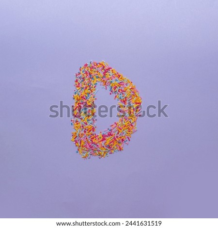 Letter D made of sugar sprinkles. Creative alphabet concept on a purple background.