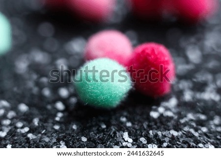 Colorful pom poms on a black glitter background. Selective focus.