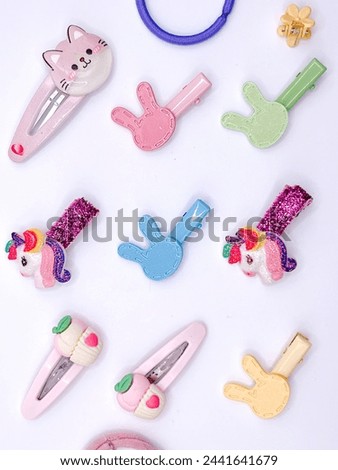 Hair clip collection featuring unicorns, rainbows, and cartoon characters arranged on a pristine white backdrop. Children’s accessory brands or playful hairstyle.