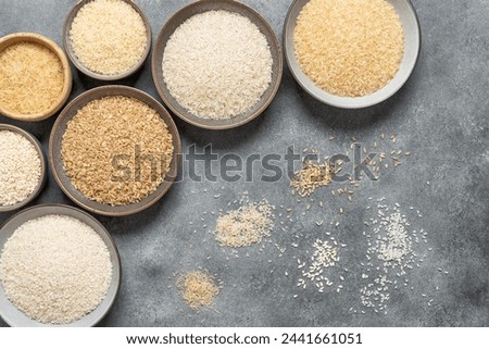 Different varieties of uncooked rice in bowls on a gray background, corner frame. Top view, flat lay, copy space.