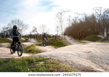 two kids on bicycles ride on a dirt jump track in bright sun under a blue sky. selective focus on jump in foreground, childs blanked out blurry in background. Family time sport concept