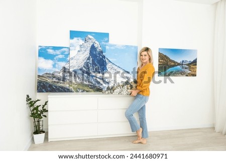 Canvas print with gallery wrap interior decor. Woman hangs landscape photography on white wall. Hands holding photo canvas print