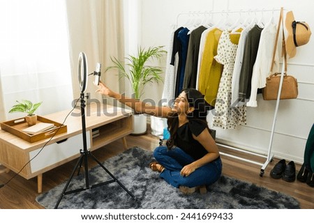 Young Hispanic woman setting up a ring light in a stylish home studio with a clothing rack