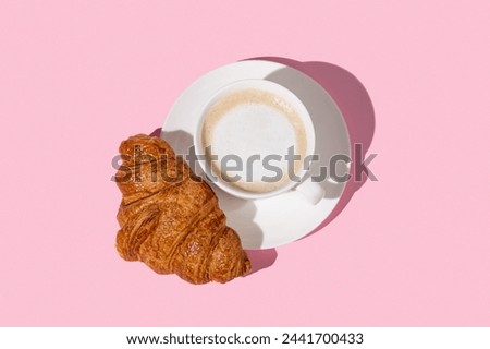 Flat lay of coffee cup and fresh croissant on a white plate on a pink background. Creative layout and concept of healthy food and french breakfast. Top view and copy space.