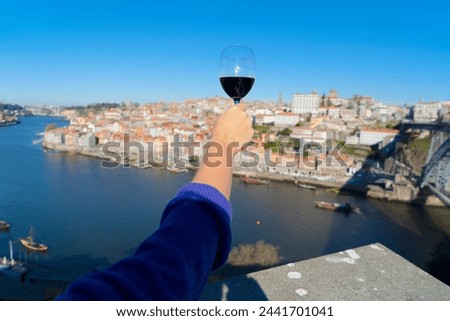 hand of woman with glass of ruby port wine on historic town of Porto, background Portugal