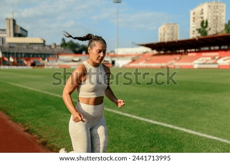 Portrait of a sportswoman in motion running at stadium on running track. A female fit athlete in shape in action. A female runner is running and jogging outdoors. Healthy lifestyle, body conscious. Royalty-Free Stock Photo #2441713995