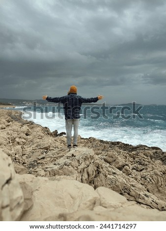 Man standing outdoors close the sea with arms out on windy day.