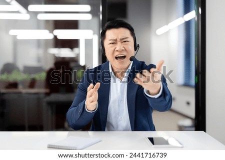 View from laptop camera of handsome asian male shouting in microphone of wireless headset while having online video call through modern gadgets. Concept of technology and business.
