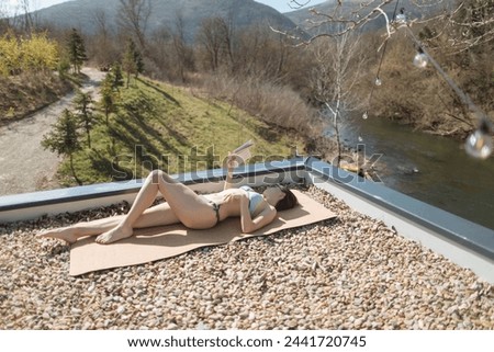 Woman sunbathing and reading a book on the terrace of countryside cottage