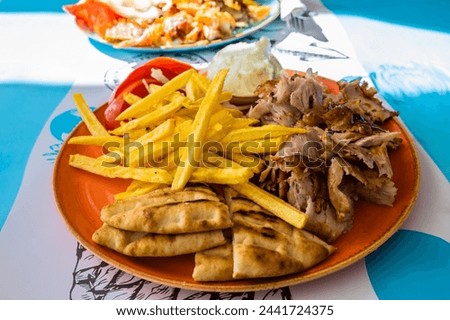 Plate with Gyros meat, pita bread, tomatoes and french fries on table in Greek restaurant, Adamas port, MIlos island, Cyclades, Greece