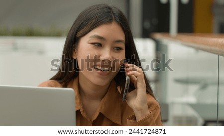 Smiling Asian woman businesswoman working online with laptop in office chinese japanese girl student freelancer talk mobile phone laughing excited female answer smartphone call carefree conversation Royalty-Free Stock Photo #2441724871