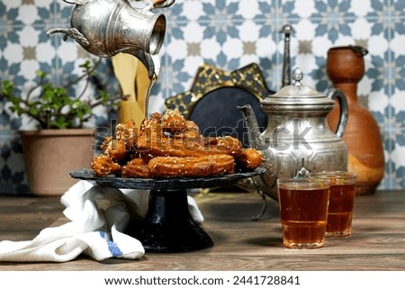 woman pouring a honey sirup on algeria oriental Balah el sham dessert fritters named zlabiat al banan in algerian language with arabic tea Royalty-Free Stock Photo #2441728841
