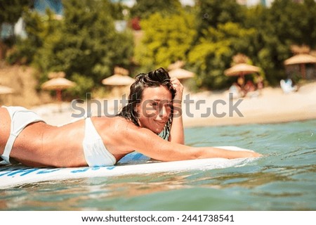 Young beautiful woman having fun swimming in the sea. Attractive tanned brunette woman swinging on the waves on a swim board