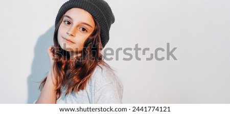 Kid fashion. Child beauty. Cute adorable hipster little girl model in black knitted beanie hat on white shadow light empty space background.