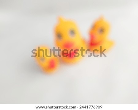 A blurry image of three cute yellow rubber duck toddler toys that are usually played with in the bath is presented on a white background