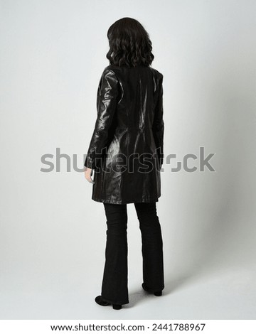 Full length portrait of brunette woman wearing long leather trench coat and black boots. Standing pose walking away from camera, facing backwards. Isolated silhouette on white studio background.