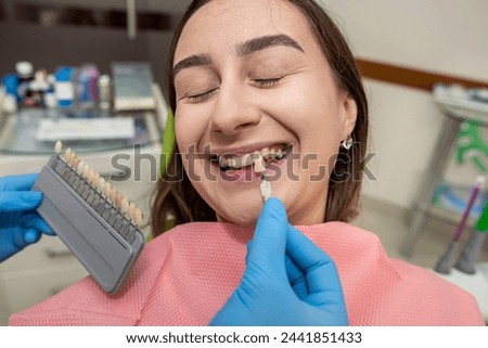 dentist doing correct tooth color with palette with shades of of beauty woman patient. Healthcare bleaching treatment Royalty-Free Stock Photo #2441851433