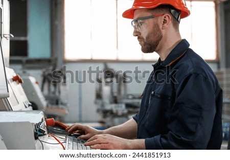 Operating the machine. Factory worker is indoors with hard hat.