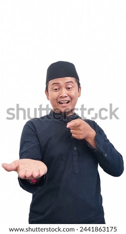 Smiling happy moslem asian man pointing something at the top side. Pointing at the left side and pointing finger at bottom side. Indonesian muslim man pointing finger his open palm showing something. 