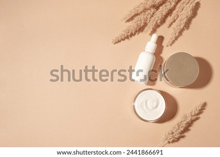 Cosmetic serum and beauty cream products with dry reeds or pampas grass on neutral beige background, trendy flat lay with hard shadows. Facial anti age natural skin care, copy space. Royalty-Free Stock Photo #2441866691
