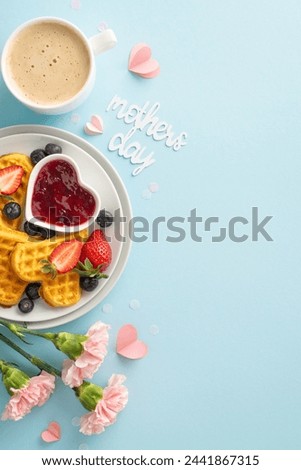 Mother's Day brunch layout: overhead vertical shot of a table with heart waffles, berries, syrup, coffee, carnations, "mothers day" note on a soft blue backdrop, space for text